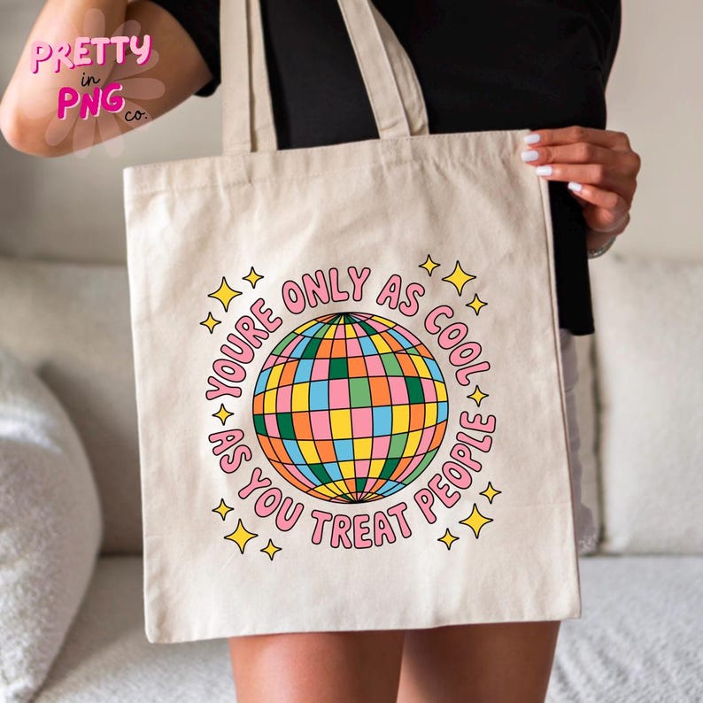 May include: Beige tote bag with a colorful disco ball graphic and the text "YOU'RE ONLY AS COOL AS YOU TREAT PEOPLE" in a pink circle. The design includes yellow star accents. The bag is held by a person.