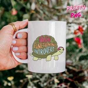 May include: White ceramic mug with a green turtle wearing pink headphones and the text "HIGH FUNCTIONING INTROVERT" in colorful letters.