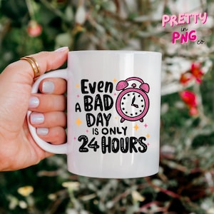 May include: White ceramic mug with a black and white graphic that says "Even a bad day is only 24 hours". The graphic also includes a pink alarm clock with black hands.