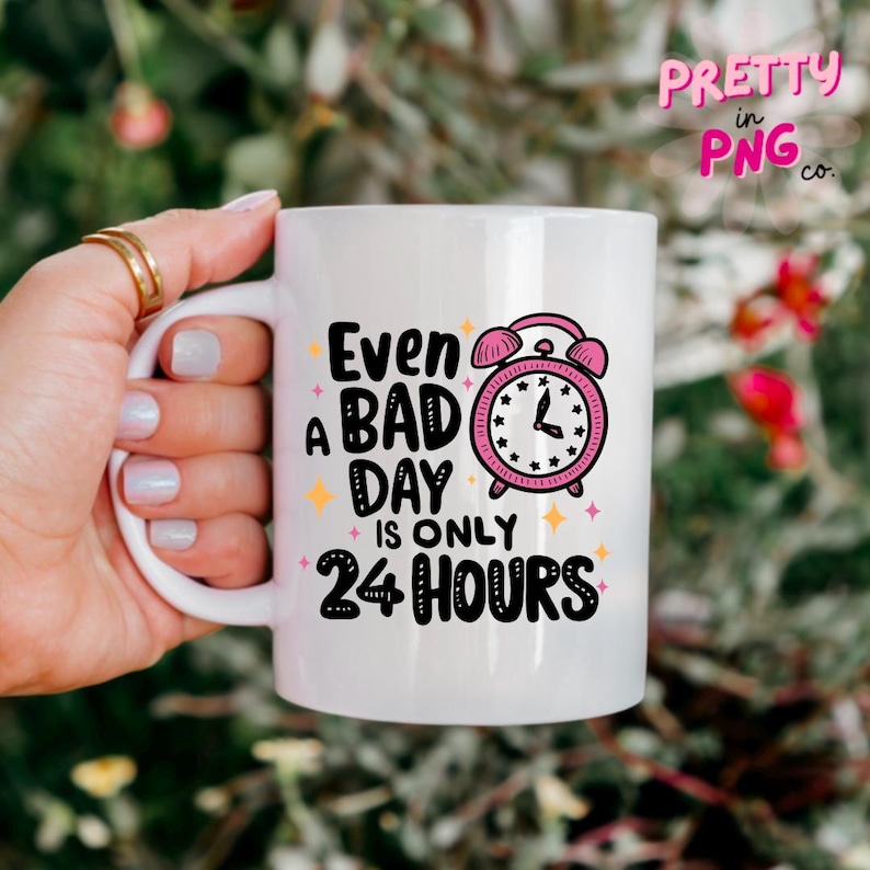 May include: White ceramic mug with a black and white graphic that says "Even a bad day is only 24 hours". The graphic also includes a pink alarm clock with black hands.