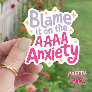 以下が含まれることがあります： テキスト「Blame it on the A-A-A Anxiety」が書かれたピンクとパープルのステッカー。テキストの周りに黄色の星が散りばめられています。