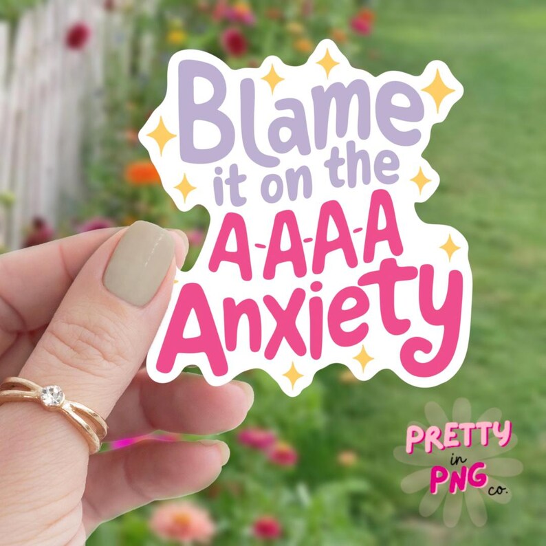 以下が含まれることがあります： テキスト「Blame it on the A-A-A Anxiety」が書かれたピンクとパープルのステッカー。テキストの周りに黄色の星が散りばめられています。