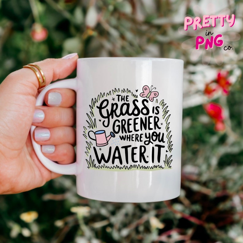 May include: White ceramic mug with a green, pink, and black design. The text on the mug reads "The grass is greener where you water it".