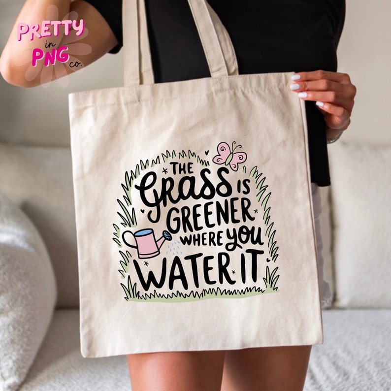 May include: A white canvas tote bag with a green grass and butterfly design. The text on the bag reads "The grass is greener where you water it."