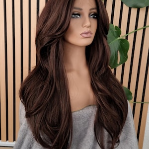 K&ouml;nnte beinhalten: Eine lange, braune, wellige Kunsthaarper&uuml;cke mit einem Spitzenfront. Die Per&uuml;cke ist mit einem Seitenscheitel und Schichten gestylt. Die Per&uuml;cke wird auf einem Mannequin-Kopf getragen.