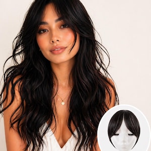 Pode incluir: Uma mulher com cabelo longo e ondulado preto e um top branco. Uma pequena imagem mostra uma peruca preta com franja. A mulher está usando um colar de ouro. O fundo é de cor clara sólida.