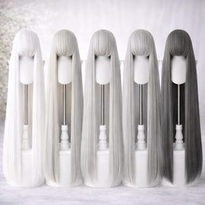 May include: Five long, straight wigs in varying shades of white, gray, and black are displayed on white mannequin heads. Each wig has a blunt bang and falls to a length below the shoulders. The wigs are arranged in a row against a white background.