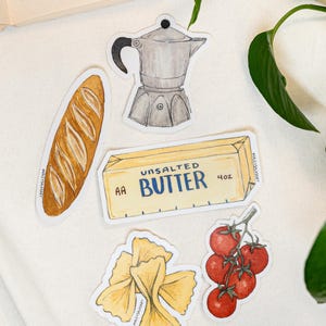May include: A collection of five die-cut stickers featuring a golden-brown baguette, a silver moka pot, a rectangular block of AA unsalted butter labeled 4oz, yellow farfalle pasta, and a cluster of five bright red tomatoes on a green vine.