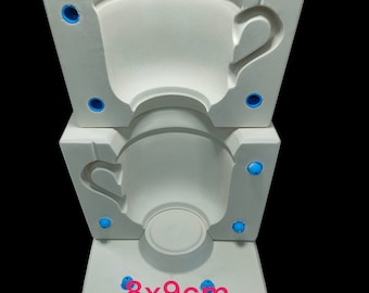 Puede incluir: Molde de cerámica blanca para hacer una taza. El molde está en tres secciones y tiene un orificio de ventilación azul en cada sección. El molde está etiquetado como "8x9cm Taza".