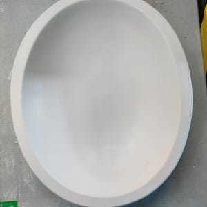 Puede incluir: Un cuenco de cerámica blanco con una superficie lisa y redondeada. El cuenco está vacío y tiene un borde ligeramente elevado.