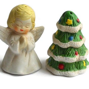 May include: A ceramic Christmas salt and pepper shaker set. One shaker is an angel figurine with closed eyes and folded hands. The other is a green Christmas tree decorated with colorful ornaments and stars.