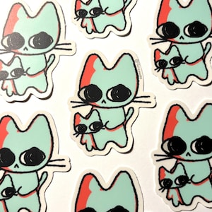May include: Multiple die-cut stickers featuring a cartoon cat holding a smaller cat. The cats are light mint green with red accents on the ears and large black eyes. The text @felixann99 is printed in small black letters on the side of the cat.