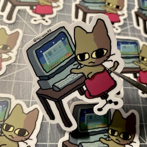 May include: A sticker featuring a cartoon cat working on a vintage computer. The cat is brown and tan, wearing a red skirt, and sitting in a chair. The computer has a gray monitor and keyboard. The sticker has a white border and the text "@felixann99".