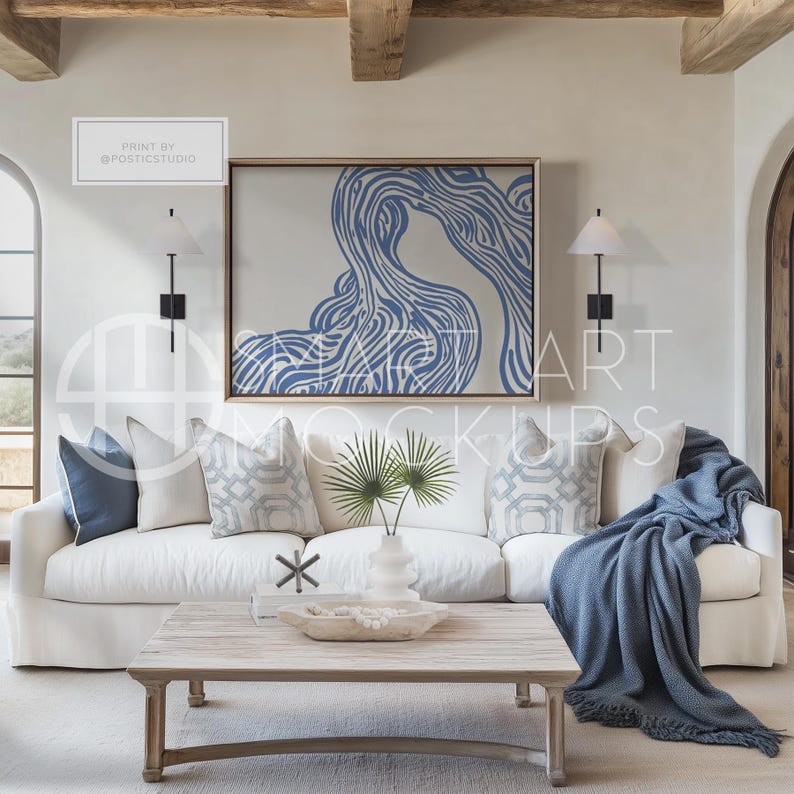 Minimalist Coastal Living Room Frame Mockup: A coastal themed mockup with a soft linen sofa, textured wood coffee table, and blank frame. Designed to show abstract paintings or landscape art, this neutral space with blue accents has a beach vibe.