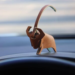 Könnte beinhalten: Eine braune Leder-Stierfigur mit einem langen, dünnen Schwanz. Der Stier steht auf einer schwarzen Oberfläche.