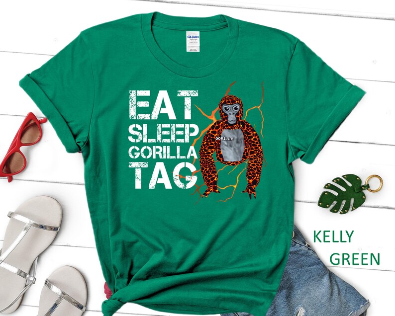May include: Kelly green t-shirt with the text "EAT SLEEP GORILLA TAG" in white block letters. A cartoon gorilla with orange and brown fur is featured on the right side. The shirt is a Gildan brand.