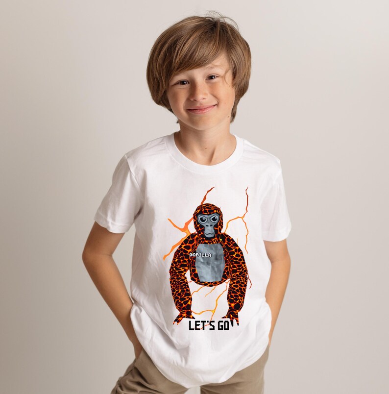 May include: White t-shirt featuring a cartoon gorilla with orange and brown fur, blue eyes, and the word "GORILLA" on its chest. The shirt also has the text "LET'S GO" at the bottom. The gorilla design is surrounded by orange lightning bolt graphics.