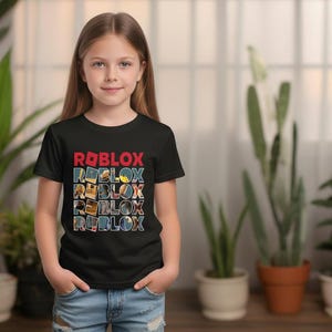 May include: A black t-shirt with the word "ROBLOX" in red and blue block letters. The shirt is being worn by a young person, and the background includes plants and a window.