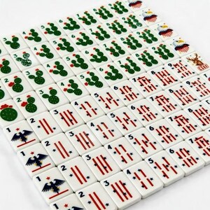 K&ouml;nnte beinhalten: Ein Set aus wei&szlig;en, rechteckigen Mahjong-Spielsteinen, die in einem Raster angeordnet sind. Die Steine zeigen gr&uuml;ne Kaktus-Illustrationen mit kleinen roten Bl&uuml;ten, rote Streifenmuster mit blauen Sternen sowie Adler-Motive und schwarze Ziffern.