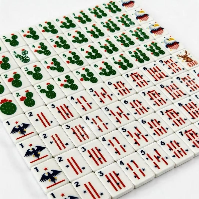 K&ouml;nnte beinhalten: Ein Set aus wei&szlig;en, rechteckigen Mahjong-Spielsteinen, die in einem Raster angeordnet sind. Die Steine zeigen gr&uuml;ne Kaktus-Illustrationen mit kleinen roten Bl&uuml;ten, rote Streifenmuster mit blauen Sternen sowie Adler-Motive und schwarze Ziffern.