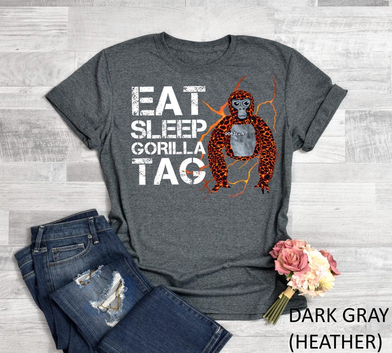 May include: Dark gray heather t-shirt with the words "EAT SLEEP GORILLA TAG" in white block letters. A cartoon orangutan with orange and brown fur is in the center. The shirt is paired with blue jeans.