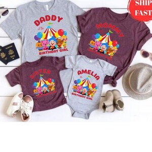 May include: Family birthday shirts in gray and burgundy, featuring a circus tent design with balloons and cartoon characters. Shirts say "Daddy", "Mommy", "Sister", and "Amelia the Birthday Girl". A baby onesie is also included.