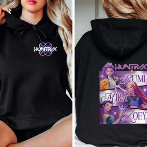 May include: Black hoodie with the text "HUNTRAX" in white and a colorful logo on the front. The back features a graphic with the names Rumi, Mira, and Zoey, along with the "HUNTRAX" logo.