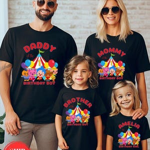 May include: Black t-shirts with colorful circus-themed graphics. The shirts feature text that reads "Daddy of the Birthday Boy," "Mommy of the Birthday Boy," "Brother of the Birthday Boy," and "Amelia the Birthday Girl."