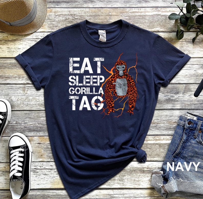 May include: Navy blue t-shirt with the text "EAT SLEEP GORILLA TAG" in white block letters. A cartoon gorilla with orange and brown fur is on the right side of the shirt. The word "GORILLA" is written on the gorilla's chest.