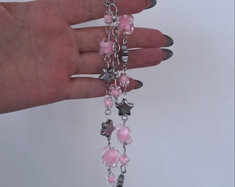 May include: A silver-toned chain bracelet featuring pink flower and star-shaped charms. The bracelet has multiple strands and a clasp closure. The charms are made of a translucent pink material and silver metal.