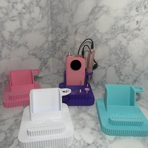 May include: A collection of colorful nail drill holders in pink, white, purple, and teal. Each holder has a rectangular base with a tiered design and a cup-like compartment. One holder contains a pink nail drill.