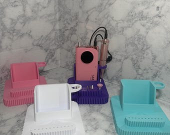 May include: A selection of nail drill holders in pink, white, purple, and teal. Each holder features a rectangular base with a tiered design and a cup-like compartment. One holder contains a pink nail drill.