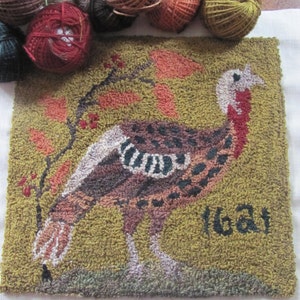 May include: A handmade, textured rug featuring a turkey design with the number "1621". The turkey is depicted in shades of brown, tan, and white, set against a green background with orange and red accents. Several balls of yarn in various colors are arranged above the rug.
