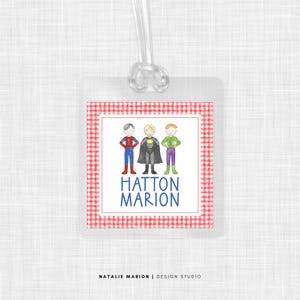 May include: A red and white gingham luggage tag with three cartoon superheroes. The tag says "Hatton Marion" in blue text.