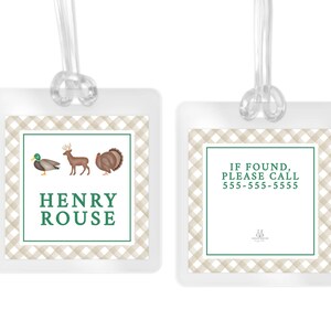 May include: Two square luggage tags with clear plastic loops. The tags feature a beige and white gingham border and a green frame. One tag displays a mallard, a deer, a turkey, and the name HENRY ROUSE. The other tag reads IF FOUND, PLEASE CALL 555-555-5555.