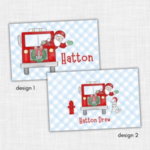 May include: Two designs of Christmas-themed cards. The cards feature a red fire truck with Santa Claus, a wreath, and the name "Hatton" or "Hatton Drew" in red. The background is a blue and white checkered pattern.
