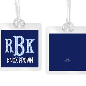 May include: Two square luggage tags with clear plastic loops. The left tag features a navy blue background with a light blue and white gingham patterned monogram RBK and the name KNOX BROWN in white. The right tag is solid navy blue.
