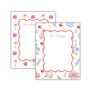 May include: Two white notepads with a school-themed design. The borders are scalloped and red. The notepads are decorated with apples, pencils, and schoolhouses. One notepad says "Ms. Robin" and the other says "Ms. Cooper".