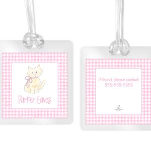 May include: Two square luggage tags with a pink and white gingham border. The left tag features a cream-colored cat illustration and the name Parker Eaves. The right tag displays the text If found, please contact: 555-555-5555. Both have clear loops.