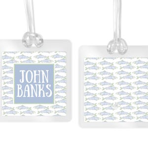 May include: Two square luggage tags with clear plastic loops. The tags feature a repeating pattern of light blue and green fish. One tag displays the name JOHN BANKS in white capital letters centered within a light blue square border.