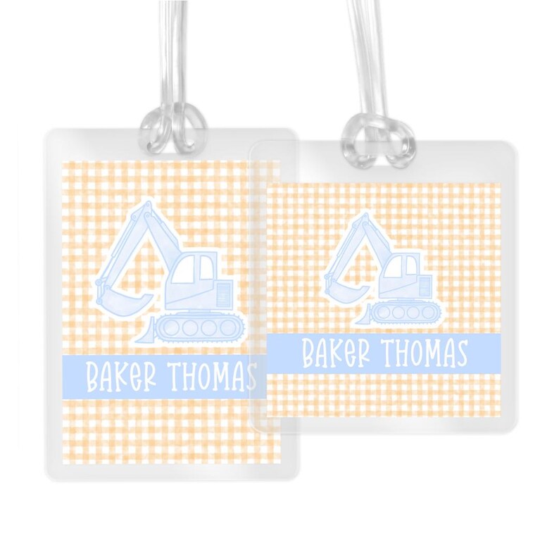 May include: Two luggage tags featuring a light blue excavator design on a yellow and white gingham background. The text "Baker Thomas" is printed on each tag.