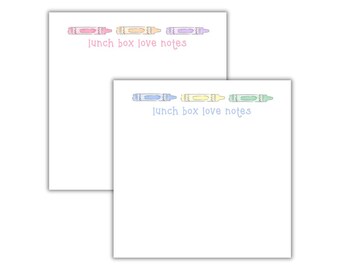 May include: Two white notepads with crayon illustrations and the text "lunch box love notes." One notepad features pink, orange, and purple crayons, while the other has blue, yellow, and green crayons. The notepads are designed for writing notes.