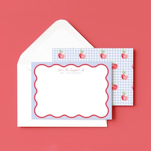 May include: A stationery set featuring a light blue card with a red scalloped border and the text "from the classroom of Ms. Appleberry". The set includes a matching envelope and a card with a gingham apple pattern.