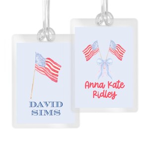 May include: Two clear plastic luggage tags with light blue backgrounds. One tag features a watercolor American flag and the name "DAVID SIMS" in blue. The other tag has two flags, a bow, and the name "Anna Kate Ridley" in red.