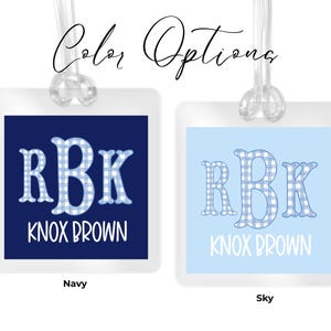 May include: Two square luggage tags with clear plastic loops. The left tag is navy blue with the white text RBK and KNOX BROWN. The right tag is sky blue with the same text. Both feature a blue and white gingham pattern on the letters RBK.