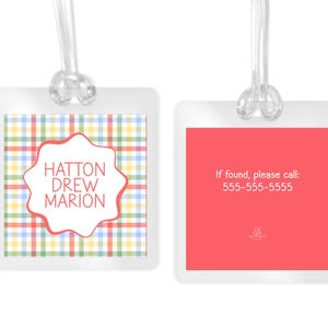 May include: Two square luggage tags with clear plastic loops. The left tag features a multicolored plaid pattern with a white scalloped center containing the text HATTON DREW MARION. The right tag is solid coral with the text If found, please call: 555-555-5555.