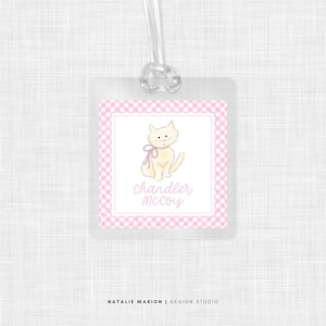 May include: A pink and white gingham luggage tag with a white cat illustration and the name "Chandler McCoy" in pink script.