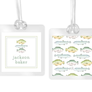 May include: Two clear, square luggage tags with a fish theme. One tag features three watercolor fish above the name "Jackson Baker" in green. The other tag has a repeating pattern of colorful fish.