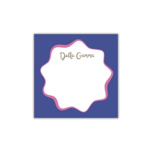 May include: A square notepad with a navy blue background and a white, wavy-edged shape outlined in pink. The words "Delta Gamma" are written in a cursive font within the white shape.