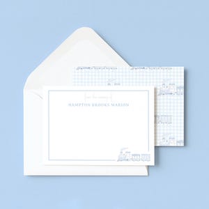 May include: A white stationery card with a blue border and a small blue train illustration at the bottom right. The text reads from the nursery of HAMPTON BROOKS MARION. The card is paired with a white envelope and a matching blue gingham liner.